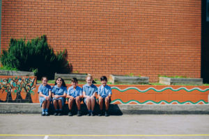 Students sitting and smiling in front of mural at St Mary Star of the Sea Catholic Primary School Hurstville